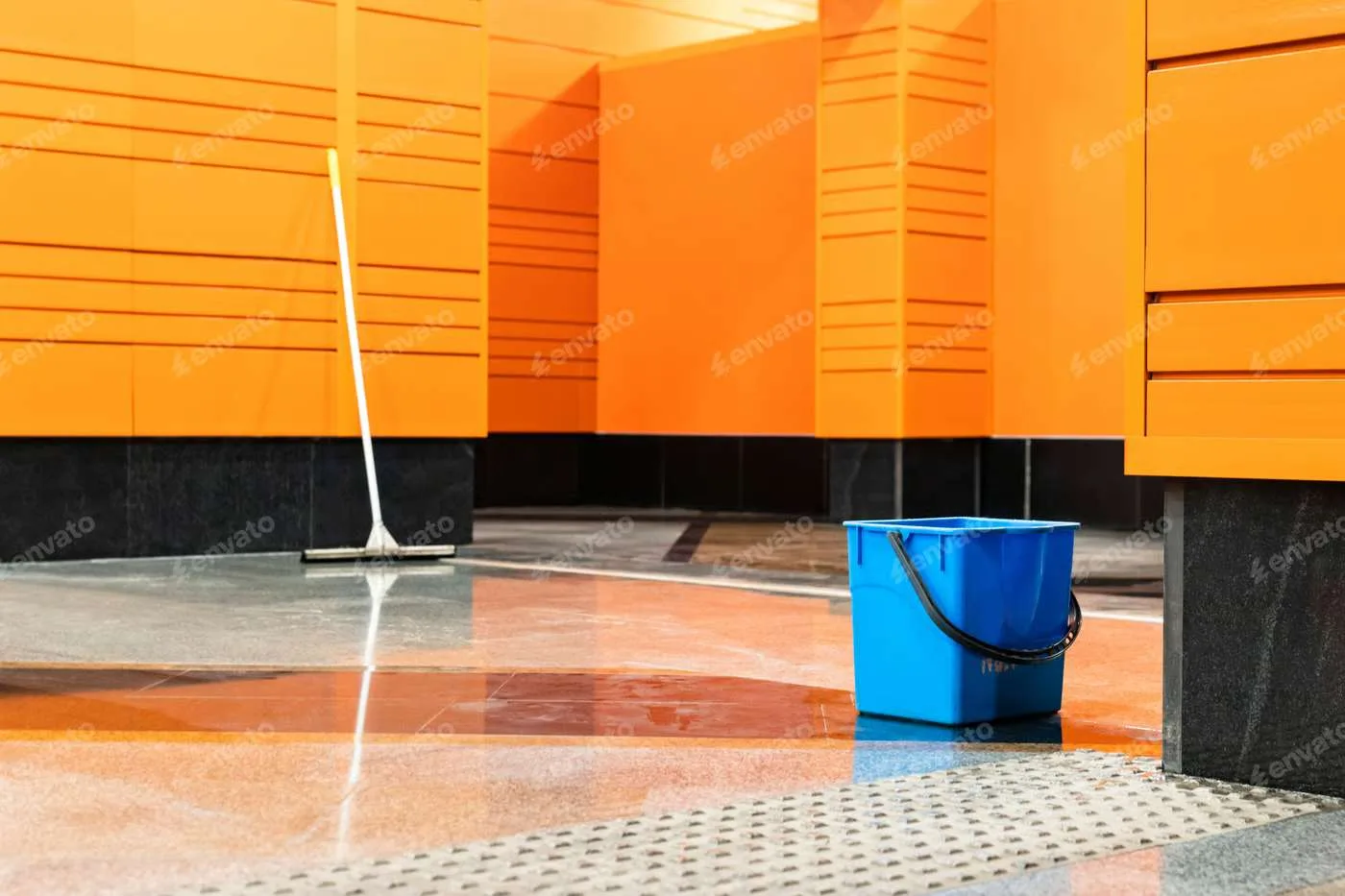 Wet floor with a squeegee and blue bucket in a brightly colored facility after a government cleaning service.