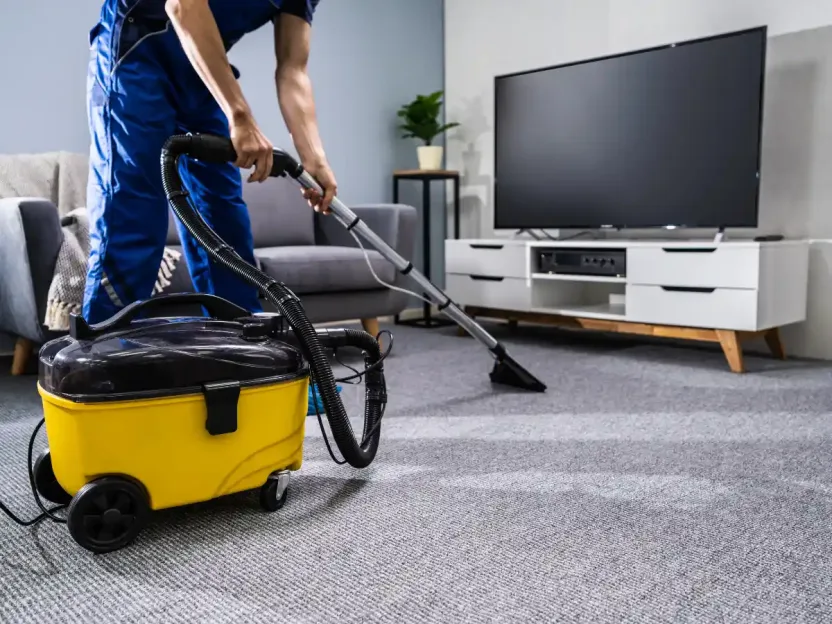 A commercial cleaner vacuums the carpet of an office's lounge area.